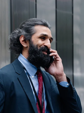 Bearded company director in a suit talking on his phone outside an office building