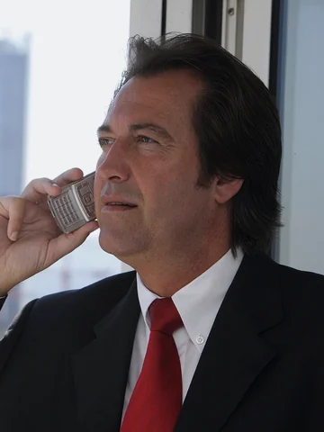 Businessman in a dark suit and red tie on a phone call by an office window